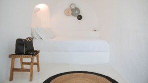 Een minimalistische slaapkamer met een bed, een klein houten krukje en een decoratief object aan de muur.