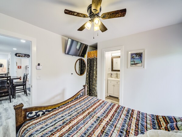 A bedroom with a bed, a ceiling fan, a TV, a bathroom, and a dining area. - Cozy Tiny Homes Yellow (Rhome)