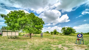A picnic area with a table and benches, a target for archery, and a tree.