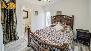 A bedroom with a wooden bed, a ceiling fan, a bedside table, and a bathroom visible through an open door.