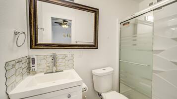 Une salle de bain avec un lavabo blanc, des toilettes, une cabine de douche en verre et un miroir doté d’un cadre décoratif.