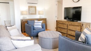 A living room with a sofa, ottoman, and a TV on a wooden cabinet. - Adorable oceanfront 2 bedroom cottage plus bunkhouse - 15 min to Charlottetown (York)