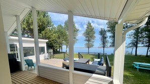 A covered deck with a view of a lake, outdoor furniture, and a grill. - Adorable oceanfront 2 bedroom cottage plus bunkhouse - 15 min to Charlottetown (York)