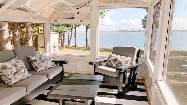 A sunroom with a view of the sea, featuring a sofa, two armchairs, and a coffee table. - Adorable oceanfront 2 bedroom cottage plus bunkhouse - 15 min to Charlottetown (York)