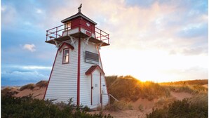 A lighthouse with a red and white exterior, situated on a sandy dune with vegetation around. - Adorable oceanfront 2 bedroom cottage plus bunkhouse - 15 min to Charlottetown (York)