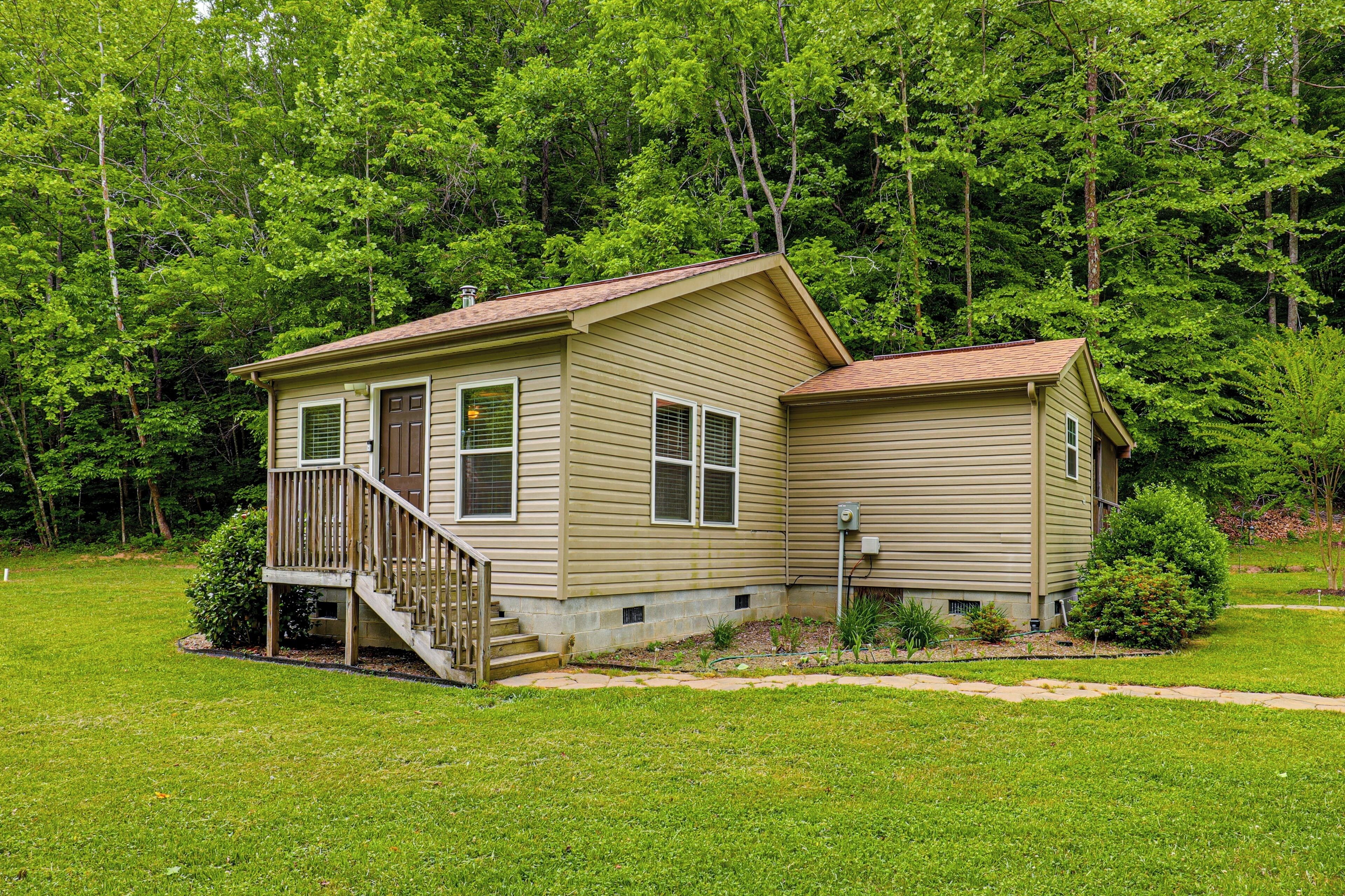 A two-story house with a deck, surrounded by a well-maintained lawn and dense forest.