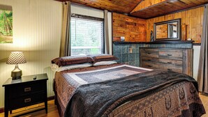 Quarto com cama, mesa de cabeceira, cômoda, espelho e janela com cortinas.
