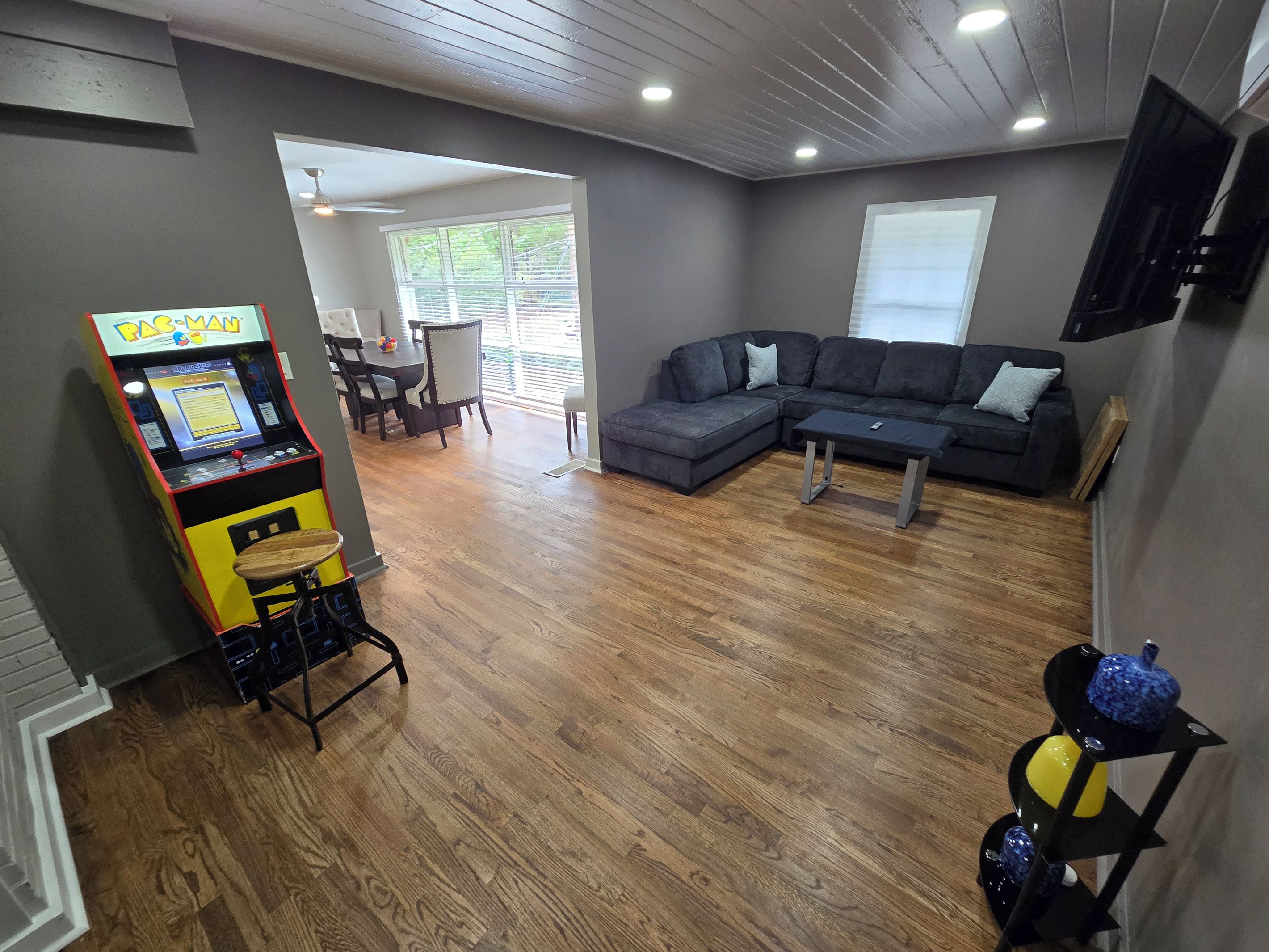 Una sala de estar con un sofá modular, una mesa de centro, una máquina arcade Pac-Man y un televisor montado en la pared.