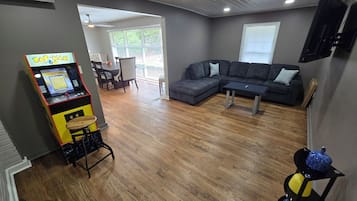 Una sala de estar con un sofá modular, una mesa de centro, una máquina arcade Pac-Man y un televisor montado en la pared.