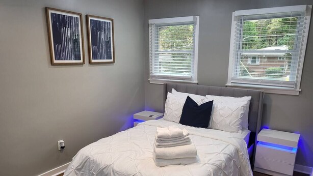 Un dormitorio con una cama, dos mesitas de noche y dos ventanas con persianas.
