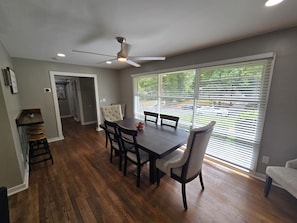 A dining area with a table and chairs, a ceiling fan, and a view through large windows.