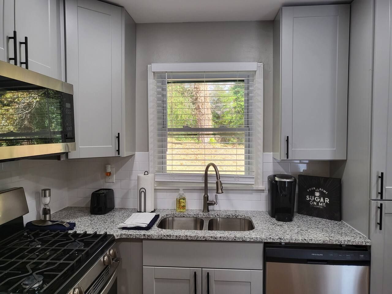 A compact kitchen with white cabinets, a double sink, a gas stove, and a coffee maker.