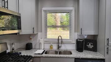 A compact kitchen with white cabinets, a double sink, a gas stove, and a coffee maker.
