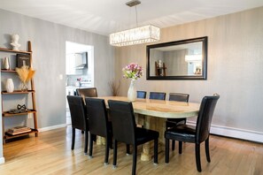 A dining area with a round table, six chairs, a vase with flowers, a chandelier, and a large mirror on the wall.