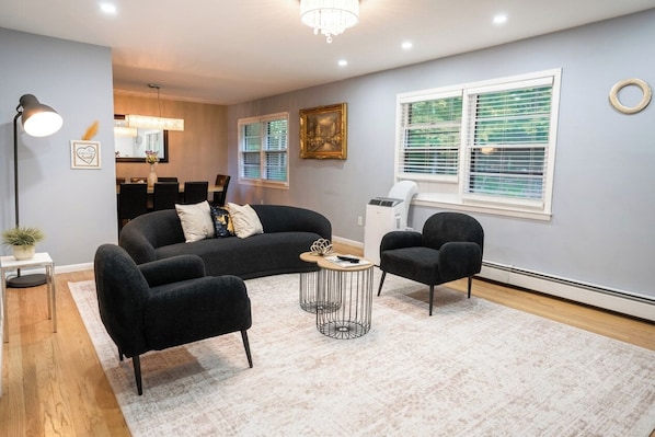 Una sala moderna con un sofá, dos sillones, una mesa de centro y una zona de comedor al fondo.