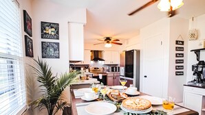 Un coin repas avec une table dressée pour quatre personnes, un ventilateur de plafond et une cuisine en arrière-plan.