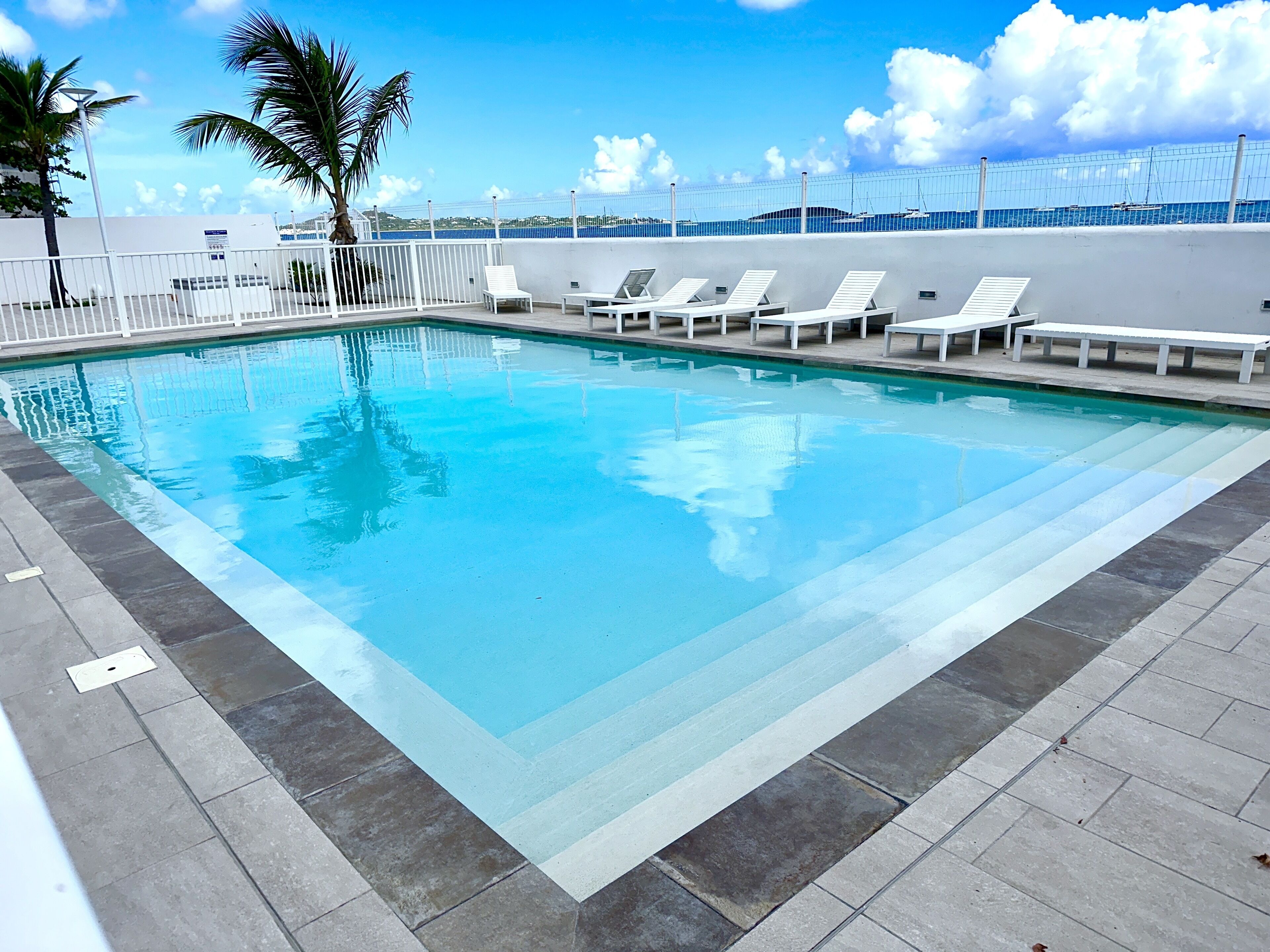 A rectangular swimming pool with white lounge chairs aligned along the edge.
