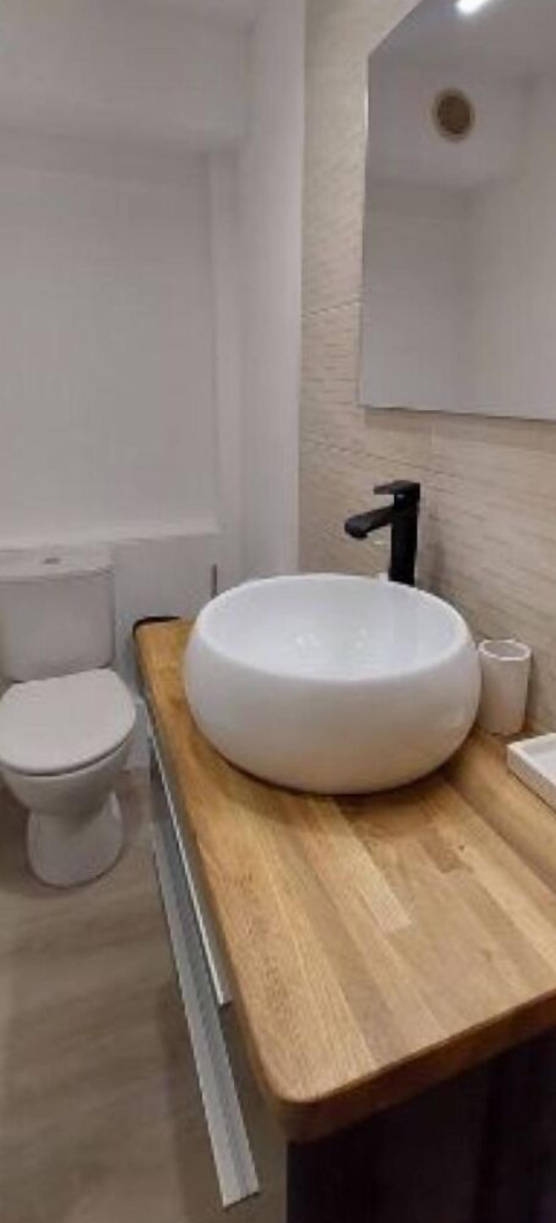 A bathroom with a white sink, a toilet, and a wooden countertop.