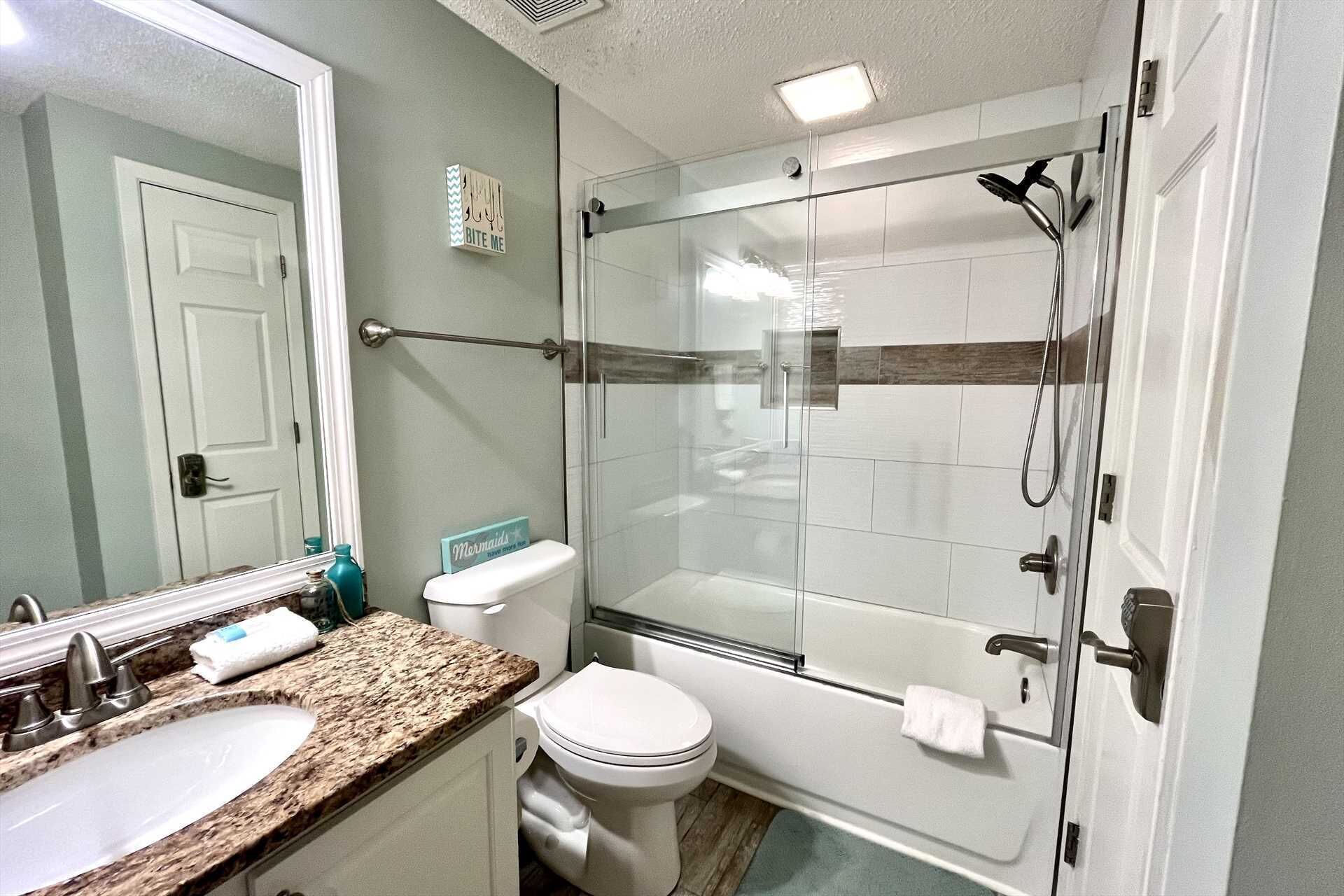 A bathroom with a glass-enclosed shower, a white toilet, a sink with a granite countertop, and a mirror above the sink.
