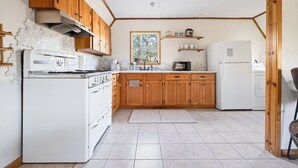 Een kleine keuken met houten kastjes, een witte kookplaat en een koelkast.