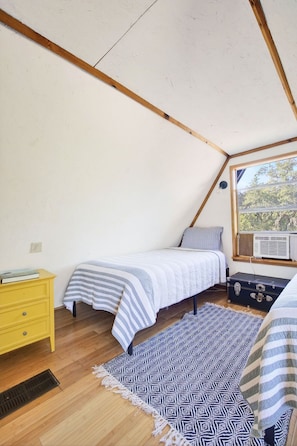 A small, triangular attic bedroom with a bed, a dresser, a window, and a patterned rug. - Kind Of Blue - A Hill Country Cottage (San Marcos)