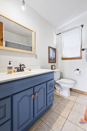 Ein Badezimmer mit einer weißen Toilette, einem blauen Waschtisch mit Spiegel und einem gerahmten Bild an der Wand.