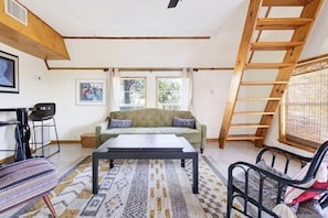 Ein Zimmer mit einer Couch, einem Couchtisch, einem Sessel, einer Leiter und einem Fenster.