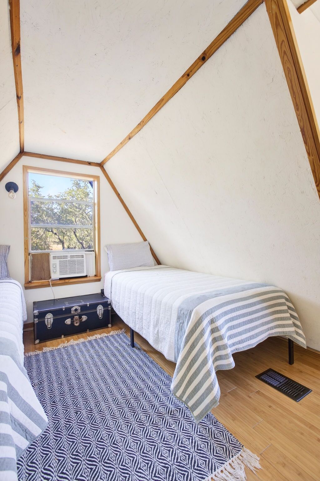 Un dormitorio ático pequeño y triangular con dos camas, una ventana y un radiador.