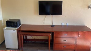 A room with a wooden desk, a television mounted on the wall, a microwave, and a refrigerator. - American Inn & Suites (Forest Park)