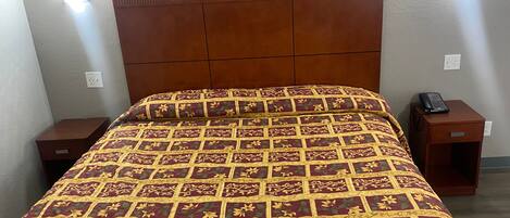 A bed with a patterned bedspread, a wooden headboard, and two bedside tables with a phone on one.