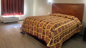 A bedroom with a large bed, a wooden headboard, a window with curtains, and a wall-mounted light. - American Inn & Suites (Forest Park)
