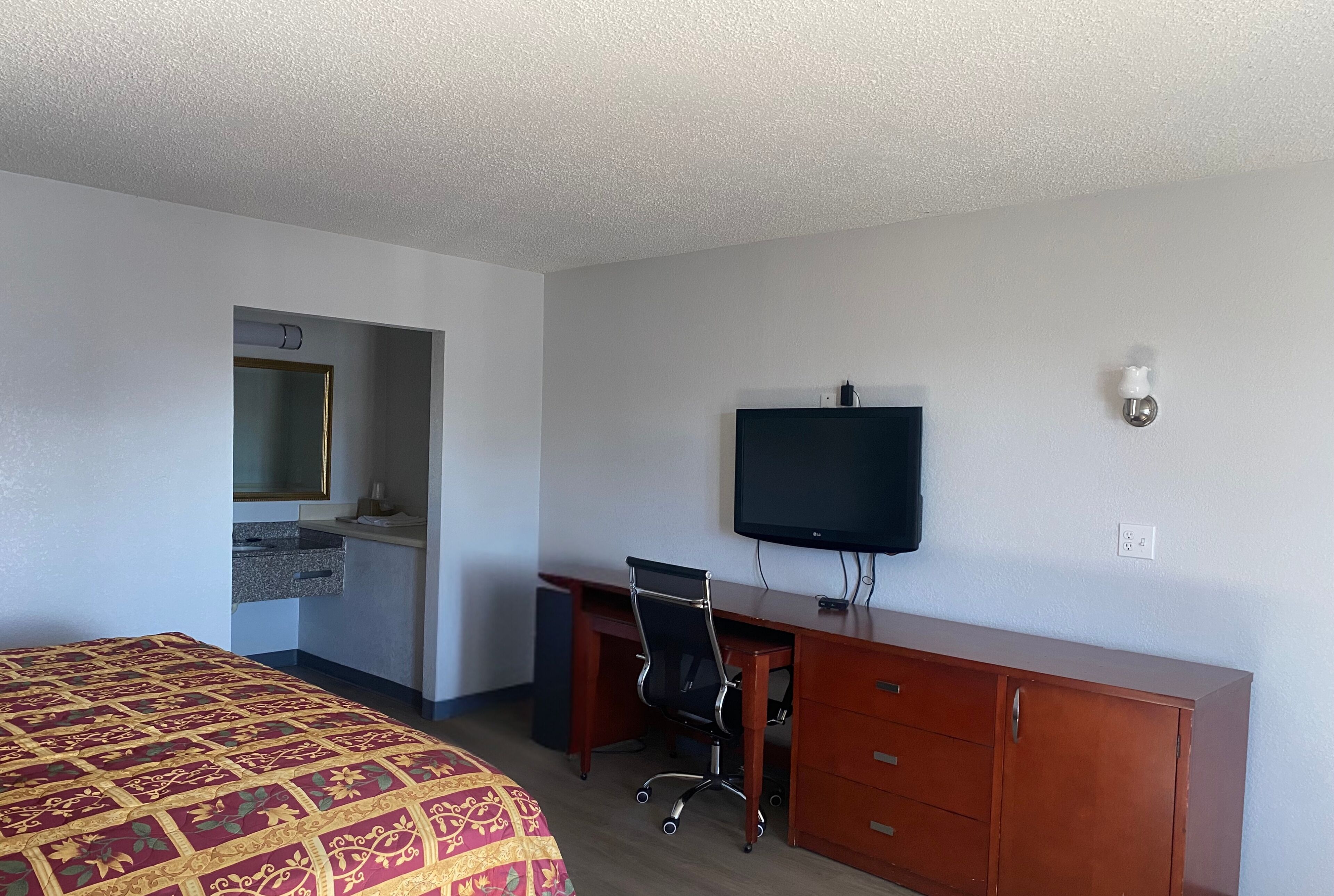 A hotel room with a bed, a desk with a chair, a television, and a small cabinet.