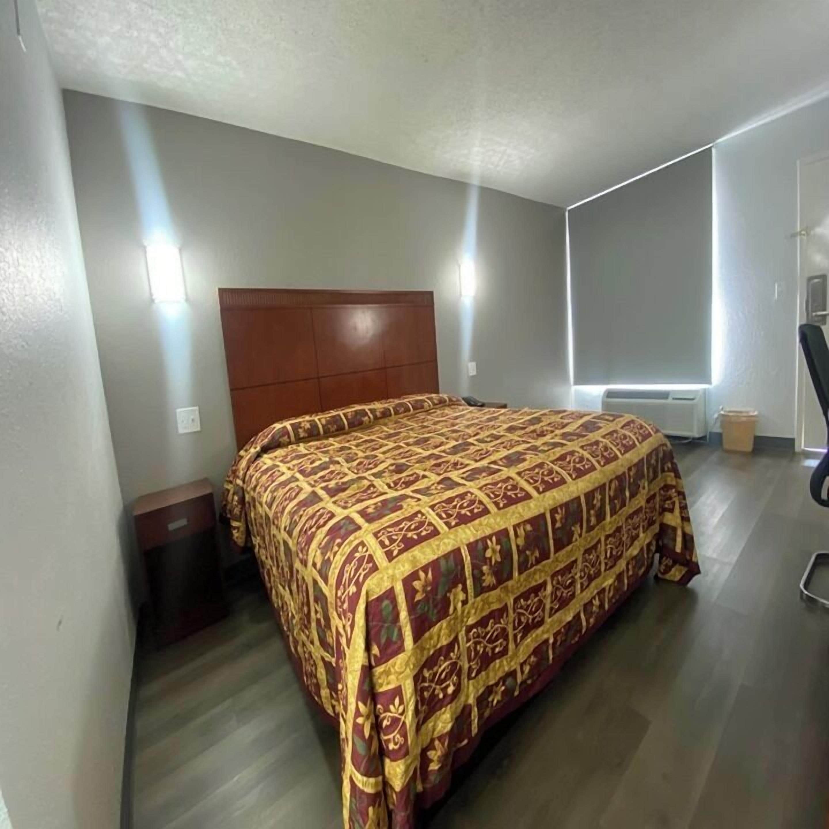 A bedroom with a large bed, a wooden headboard, a nightstand, a chair, and a window with blinds.