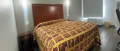 A bedroom with a large bed, a wooden headboard, a nightstand, a chair, and a window with blinds.