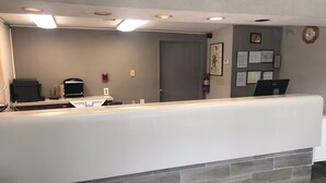 A reception area with a white counter, a fire alarm, a clock, and a Dell laptop on the wall. - American Inn & Suites (Forest Park)