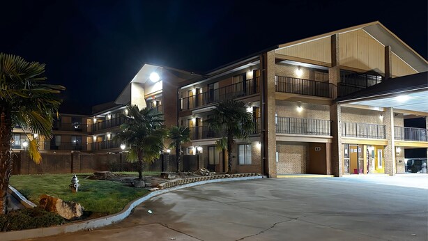 A multi-story hotel with a covered parking area and a well-lit entrance. - American Inn & Suites (Forest Park)