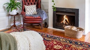 A cozy living room with a fireplace, a red leather armchair, a patterned rug, and a side table with a plant.