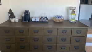 A coffee station with a Keurig machine, cups, and a water dispenser on a wooden counter.