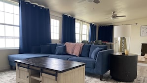 A living room with a sectional sofa, a wooden coffee table, a black side table, and a patterned rug.