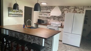 A kitchen with a central island, bar stools, a microwave, stove, and a refrigerator.