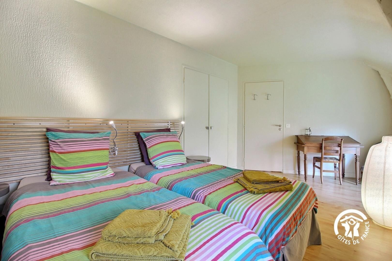A bedroom with two beds, striped bedding, a wooden headboard, a desk, and a chair.