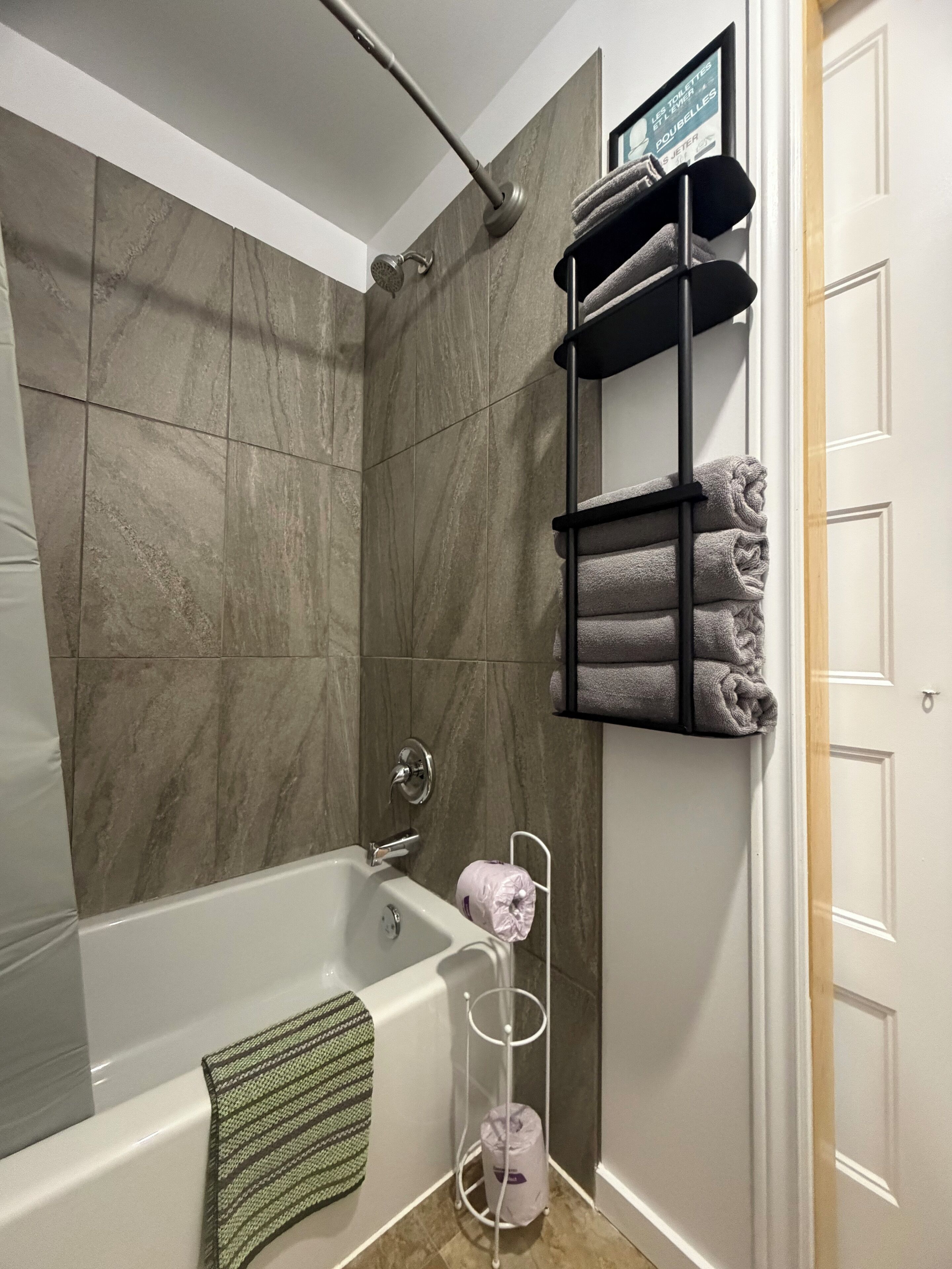 A modern bathroom with a bathtub, a towel rack with folded towels, and a toilet paper holder.