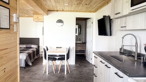 Cocina compacta con armarios de madera, un lavamanos y un microondas. Hay una zona de comedor con una mesa y sillas.