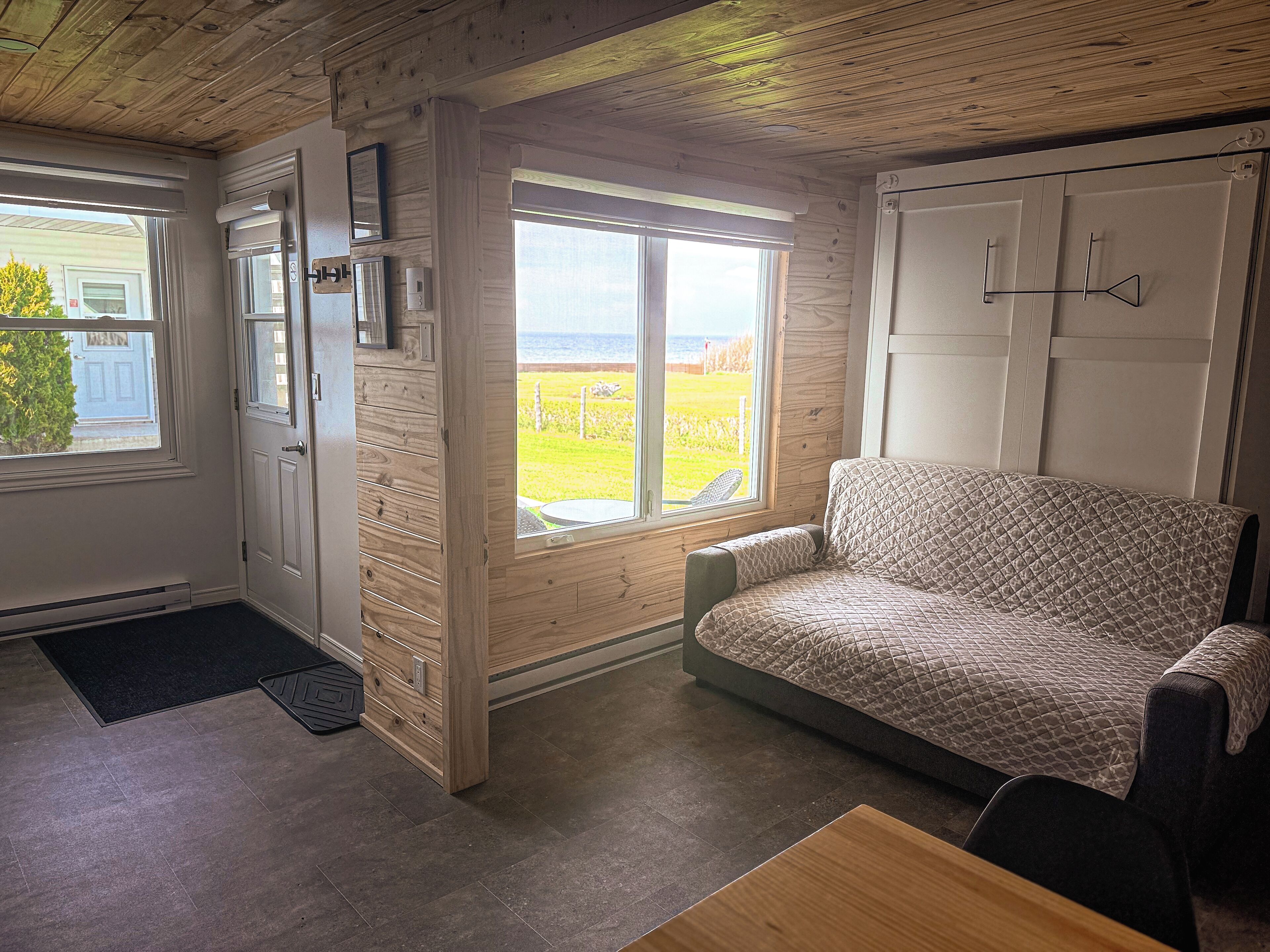 Une pièce chaleureuse avec un plafond en bois, un canapé, une table et une vue sur un champ verdoyant par la fenêtre.