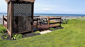 Un área de picnic de madera con bancos y una estructura de celosía, con vistas a una playa.
