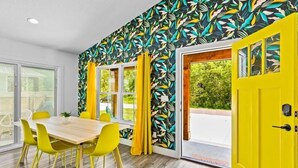 Una habitació amb taula de dinar de fusta i cadires grogues, una porta de color groc brillant i una finestra amb cortines.
