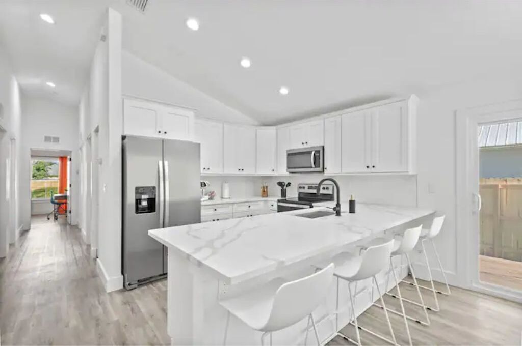 A modern kitchen with white cabinetry, a large island with bar stools, a built-in microwave, and a stainless steel refrigerator.