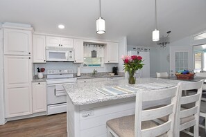 A kitchen with white cabinetry, a granite countertop, a central island with seating, and pendant lighting. - 383 East Lake Cottage in Oceanside Village (Surfside Beach)