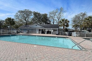 Relax by the pool surrounded by lush greenery and a brick patio.