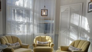 A cozy room with a high ceiling, a yellow armchair, a matching armchair, and a small table with a rug. - Room 2 - The Inn at Dirickson Creek (Frankford)